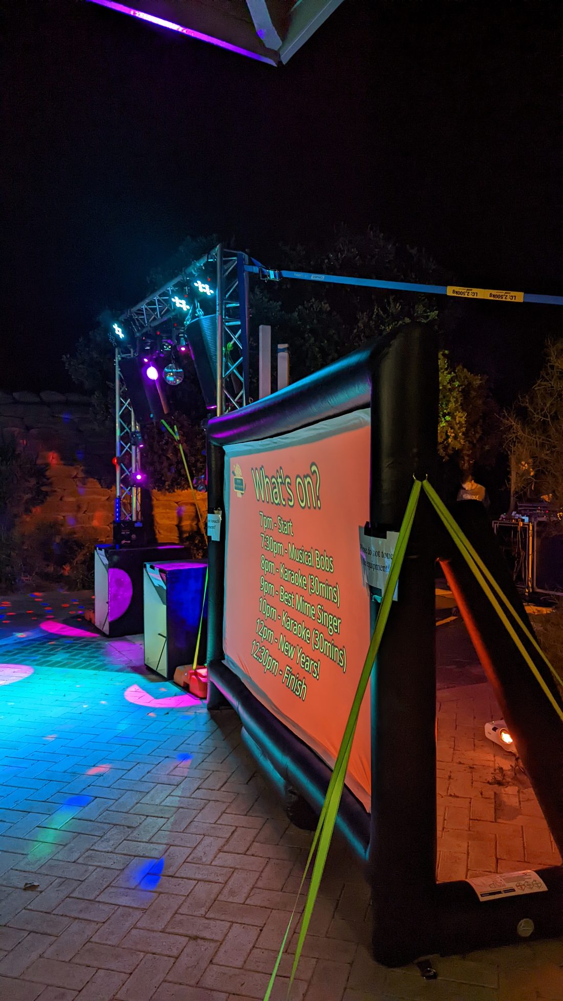 Perth Pop-Up Movies New Year's Eve setup at Woodman Point Caravan Park, 2021, inflatable cinema screen showing the night's run sheet beside a lighting rig and mirror ball
