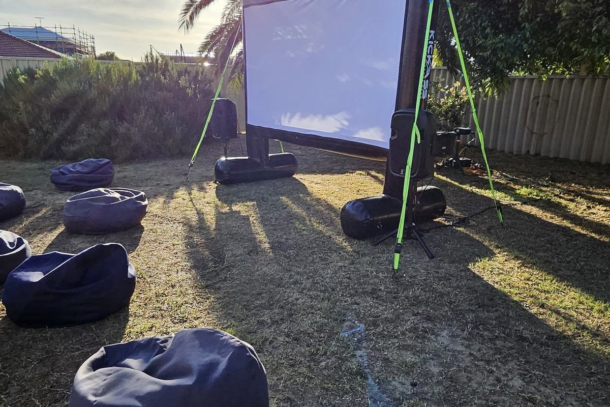 3m inflatable outdoor cinema screen set up in a Perth backyard at sunset with bean bags
