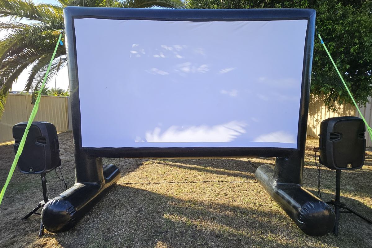Outdoor cinema screen, projector and PA speakers set up on grass for a Perth event